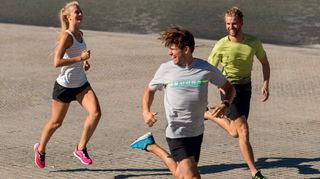 Three people running, the person at the front is looking behind him and smiling