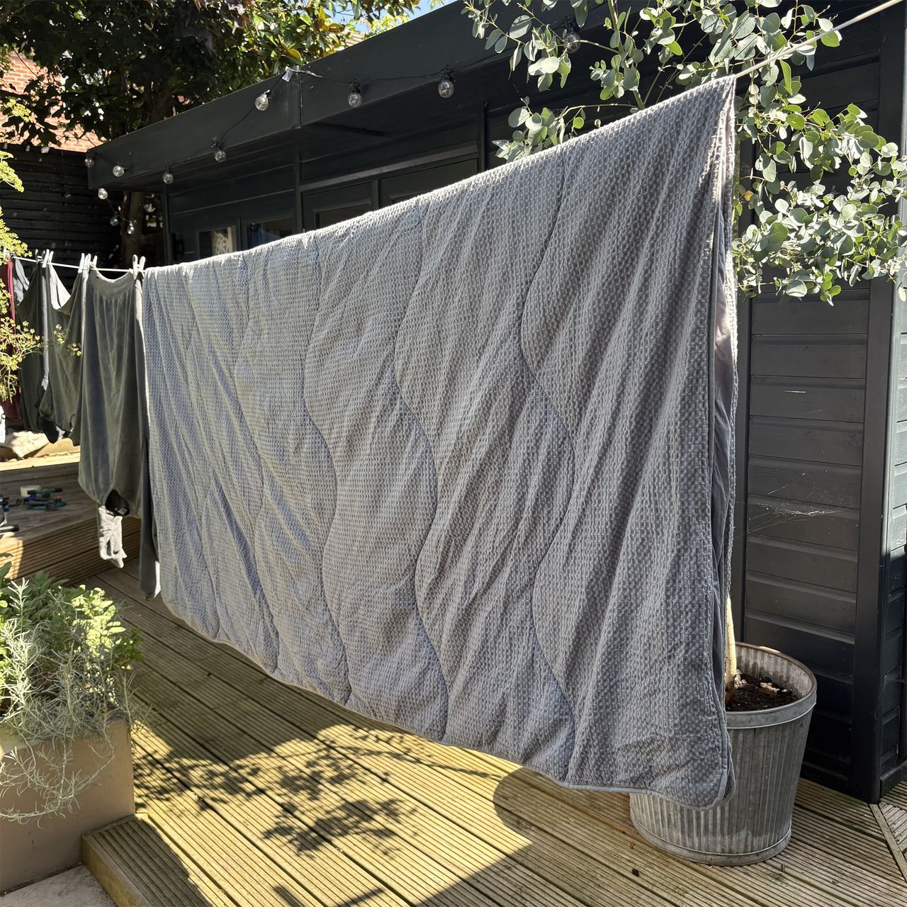 A grey coverless duvet hanging on the washing line in the garden