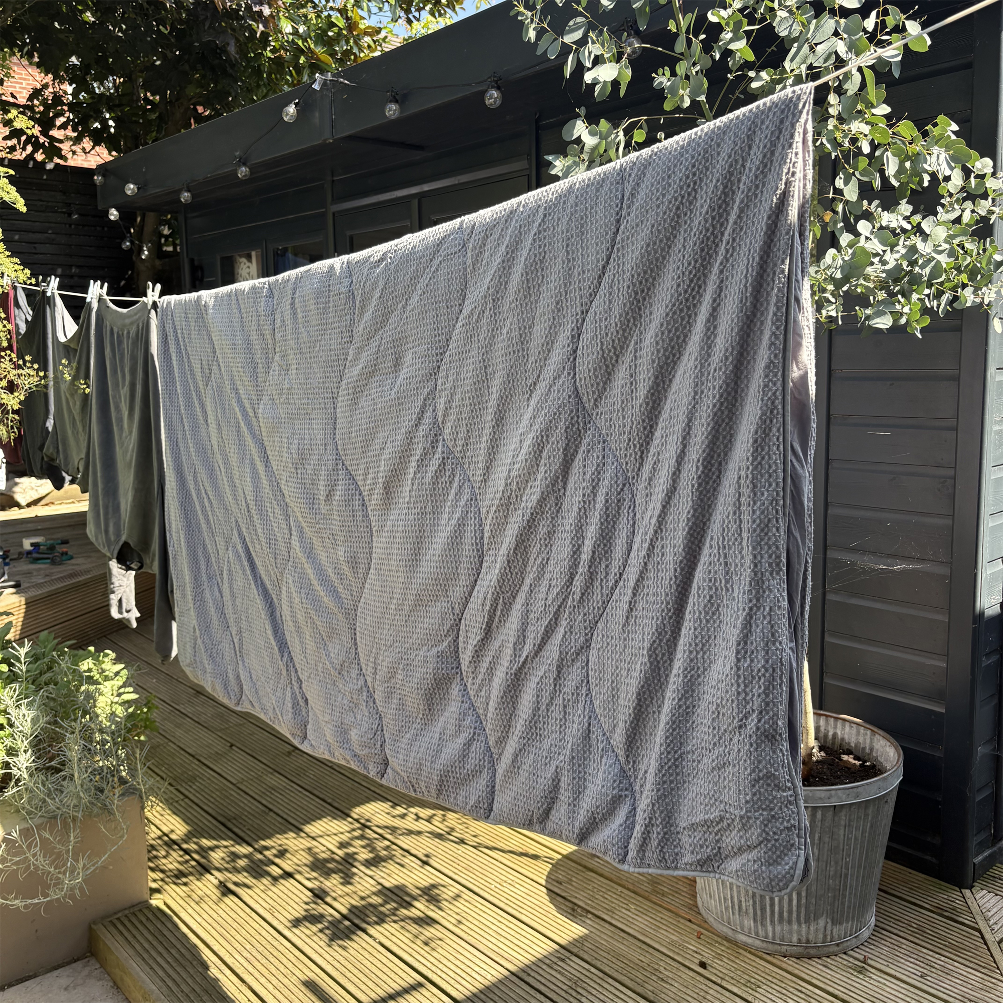 A grey coverless duvet hanging on the washing line in the garden