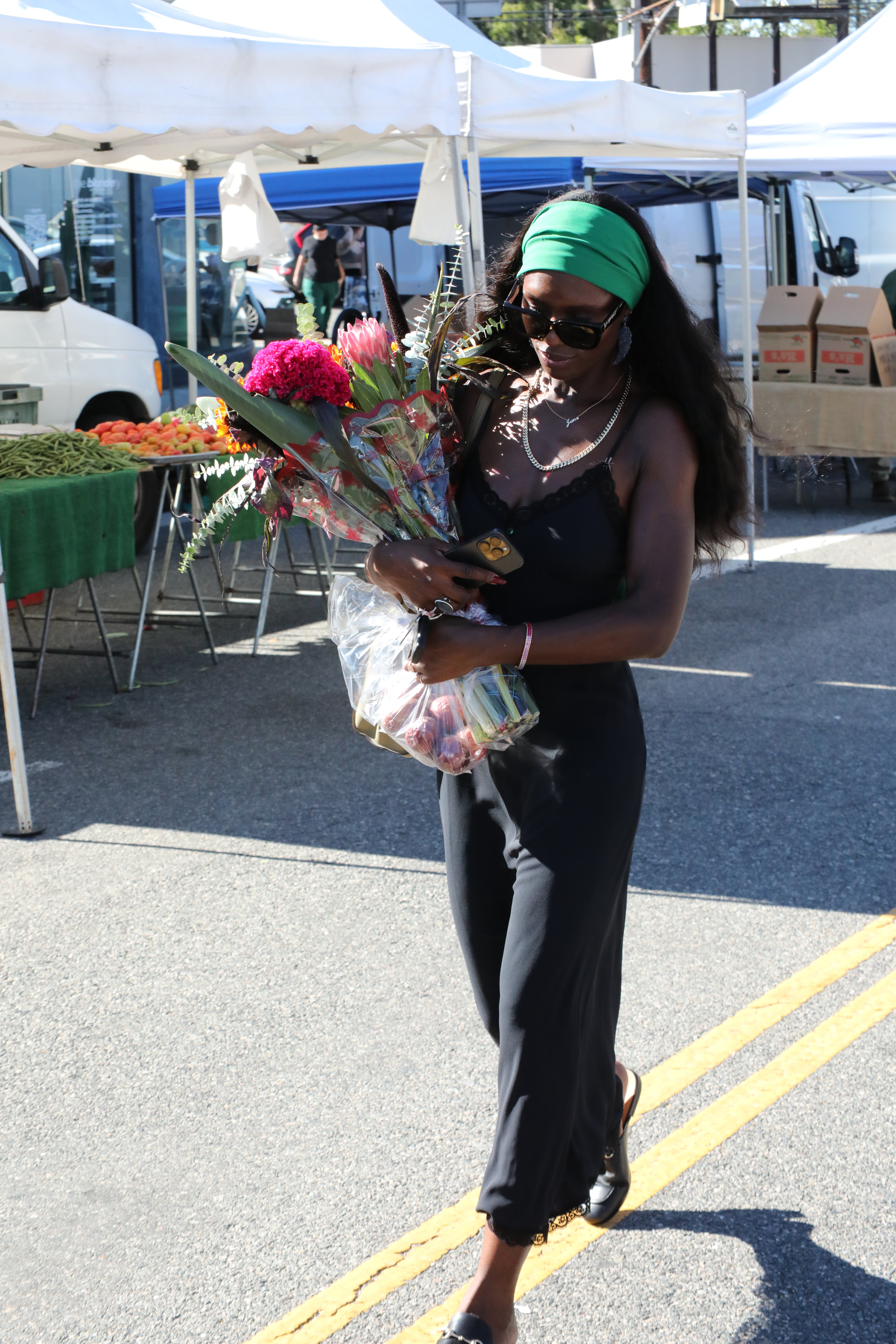 Jodie Tuner Smith wearing a wavy hairstyle and a green headband. She is also wearing a black dress and loafers, and holding flowers in her hand