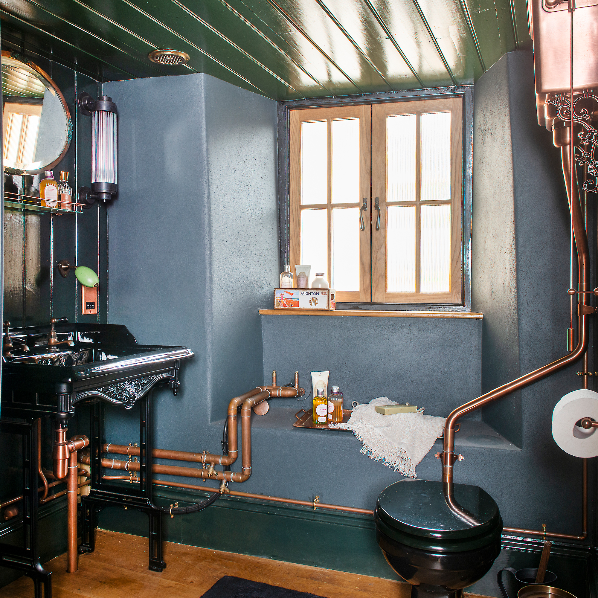 Dark panted bathroom with exposed copper pipes, black vanity and toilet and copper cistern