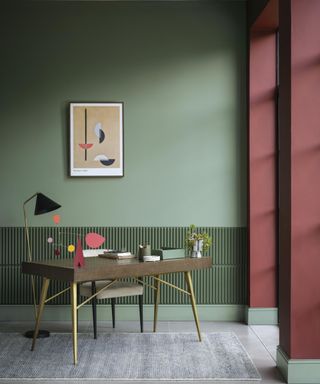 green office room with wooden desk, artwork on wall and dark red dooway