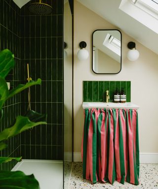 bathroom with dark green tiles in shower enclosure, pink and green striped curtain around base of sink unit