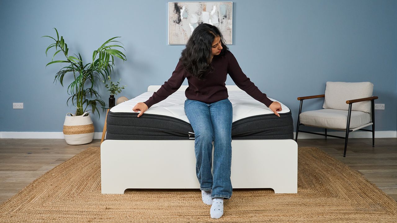 Mattress tester Becky George sits on the edge of the Plank Firm Luxe mattress. The mattress does bow beneath her but she looks comfortable and stable