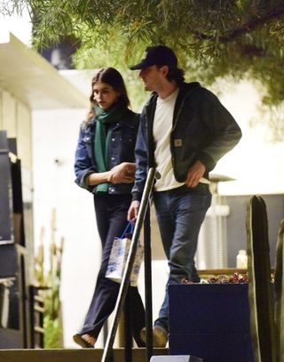 A photo of Kaia Gerber wearing a dark wash jean jacket, black pants, black Repetto ballet flats, and an emerald green scarf to celebrate Lewis Pullman's birthday.