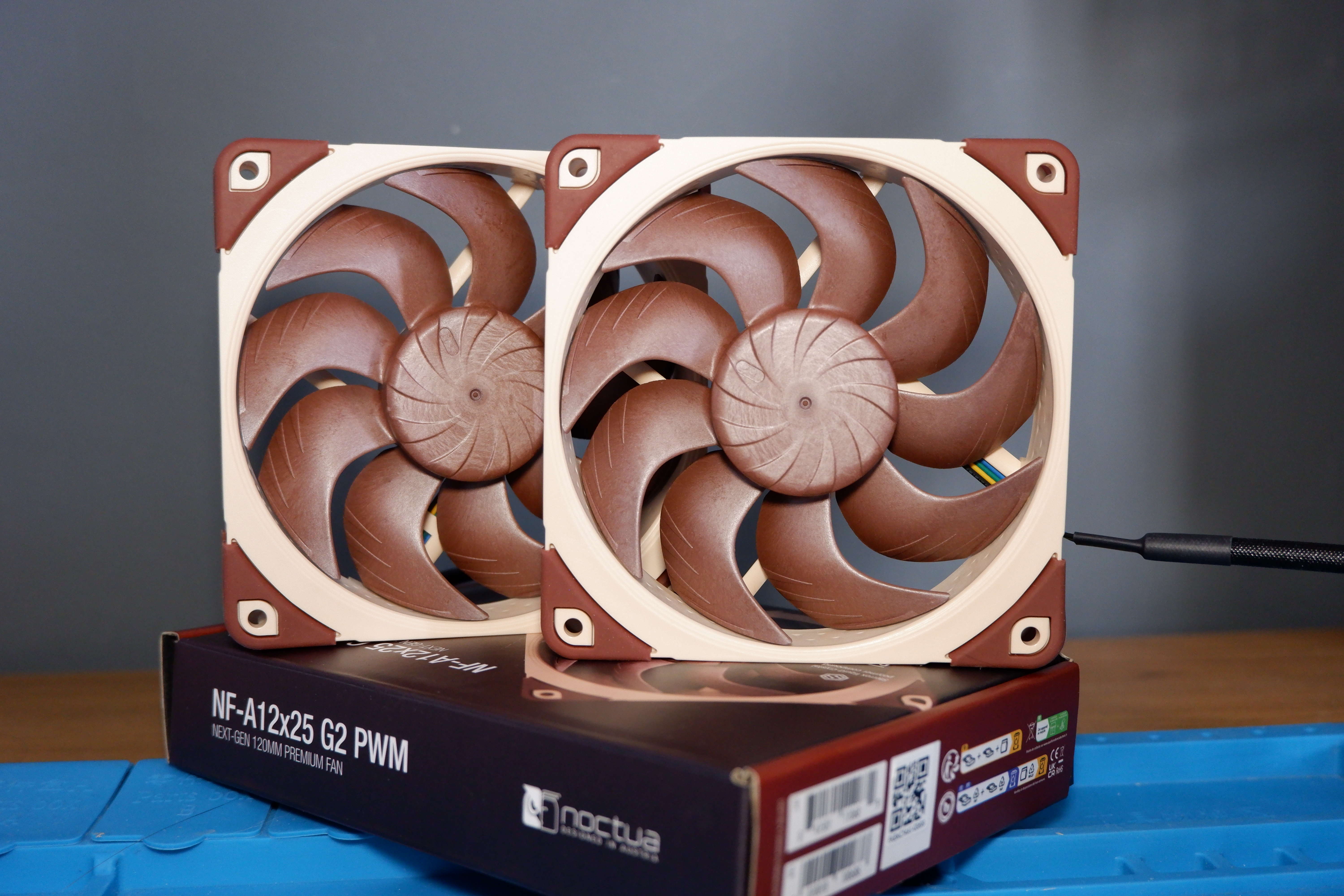 A set of Noctua NF-A12x25 G2 PC fans on a desk with packaging.