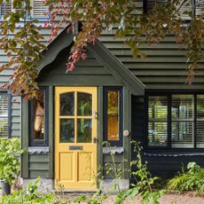 exterior of woodclad house painted dark olive green with yellow front door on porch