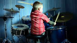 Child in a red stripy shirt plays a blue drum kit