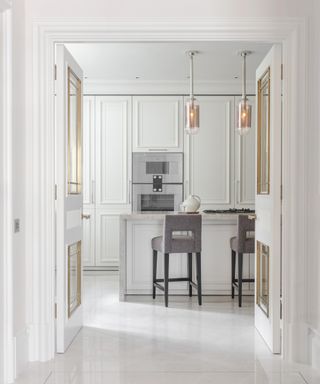Modern white kitchen ideas with white polished stone floor and island visible through kitchen's double white doors