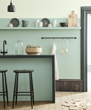 Pale green and black kitchen with a two tone wall and wooden flooring.