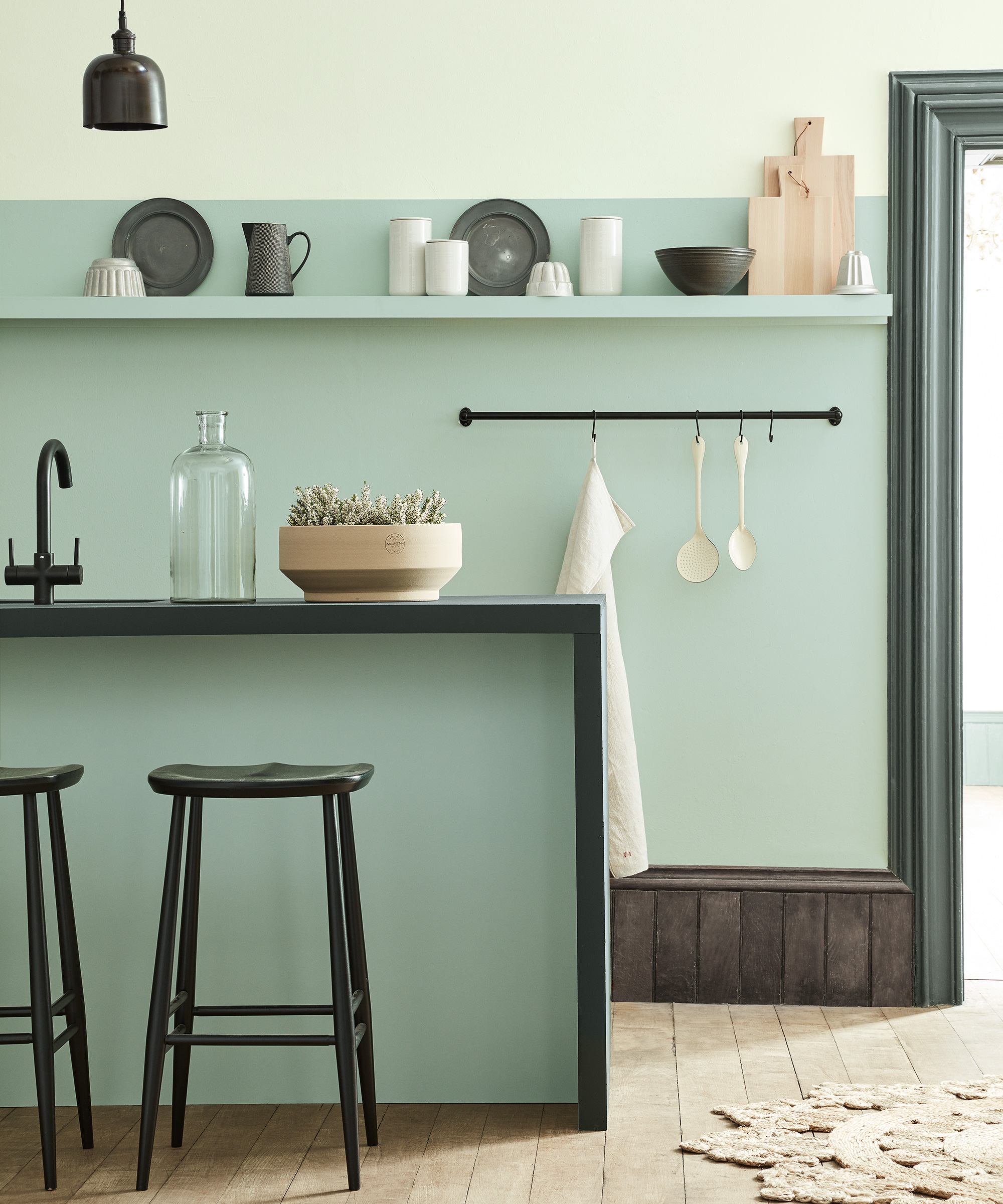 Pale green and black kitchen with a two tone wall and wooden flooring.