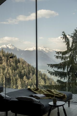 A hotel room boasts sweeping views of a mountain range blessed by sunshine thanks to its floor-to-ceiling walls and minimally furnished interiors.