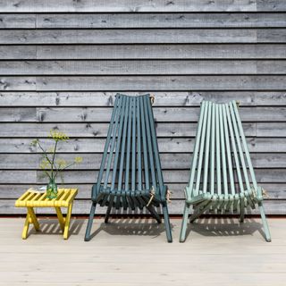 Blue garden chairs and small yellow table painted in Protek paint on wooden decking area next to wooden fence in garden