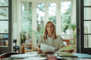 Hannah (Lesley Sharp) sits at a desk in her house sifting through paperwork with a solemn look on her face