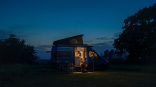 Couple glamping in van on grassy patch at night under sunset