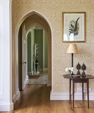 A hallway wallpaper idea with neo gothic arch, yellow and white wallpaper and entry table