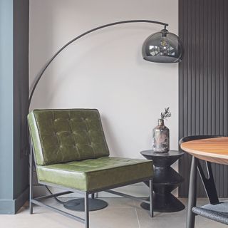Living room with vintage-inspired green armchair and curved stainless steel standing lamp.