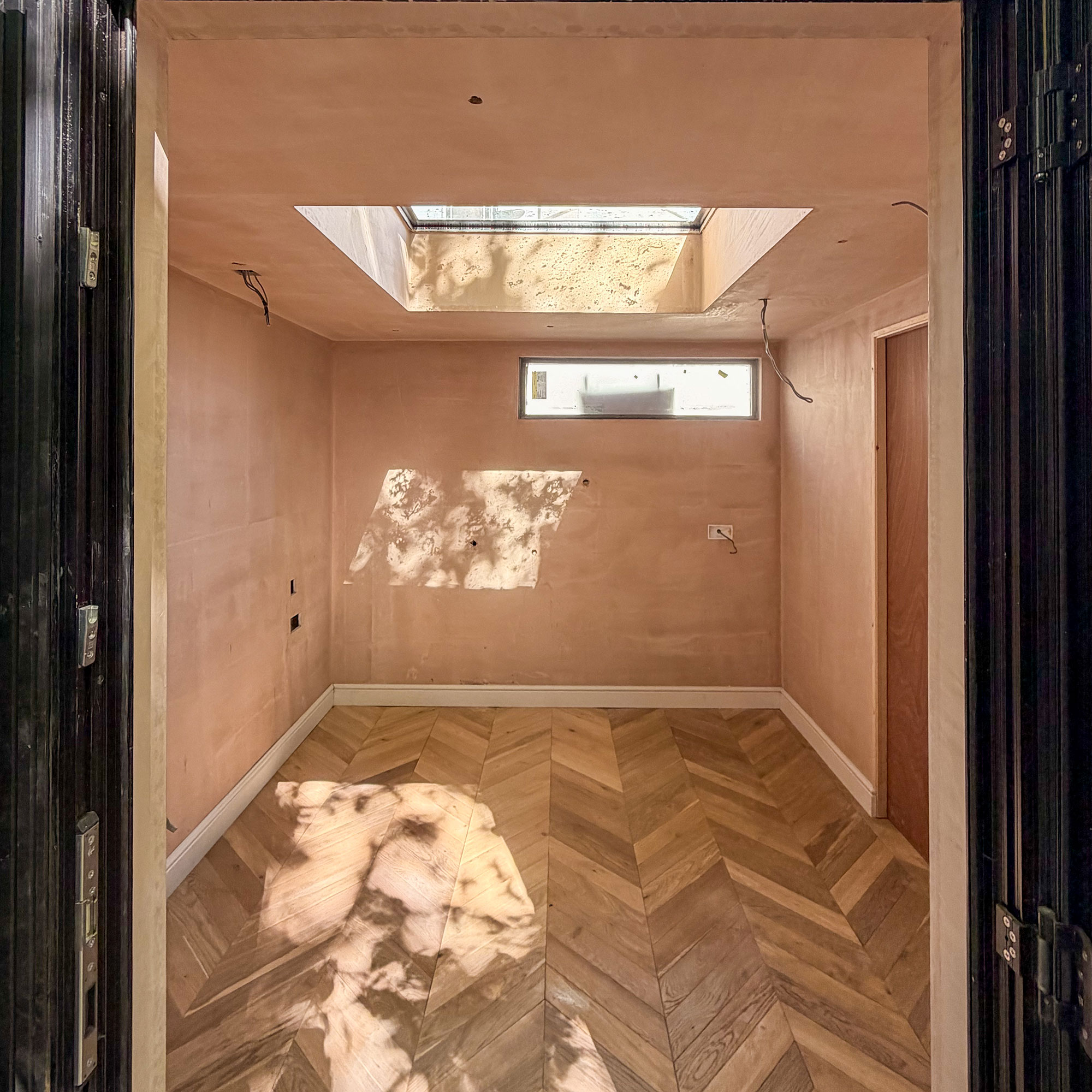 Empty room mid renovation with plaster walls, wooden parquet and rooflight