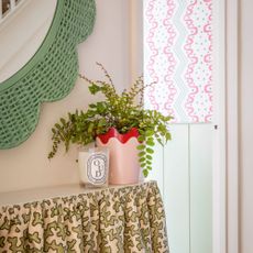 button fern in red and pink pot next to candle on shelf covered by decorative cloth