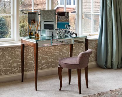 An example of dressing table ideas showing a mirrored dressing table in front of a window with an upholstered chair