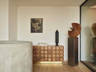 A living room with a wooden floors, a wooden credenza with a gold base, and a wooden sculpture