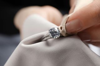 A close up of a jewellery cleaning a diamond ring with a microfibre cloth.