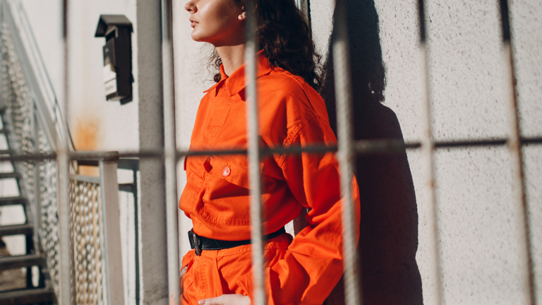 Woman in orange jumpsuit behind bars