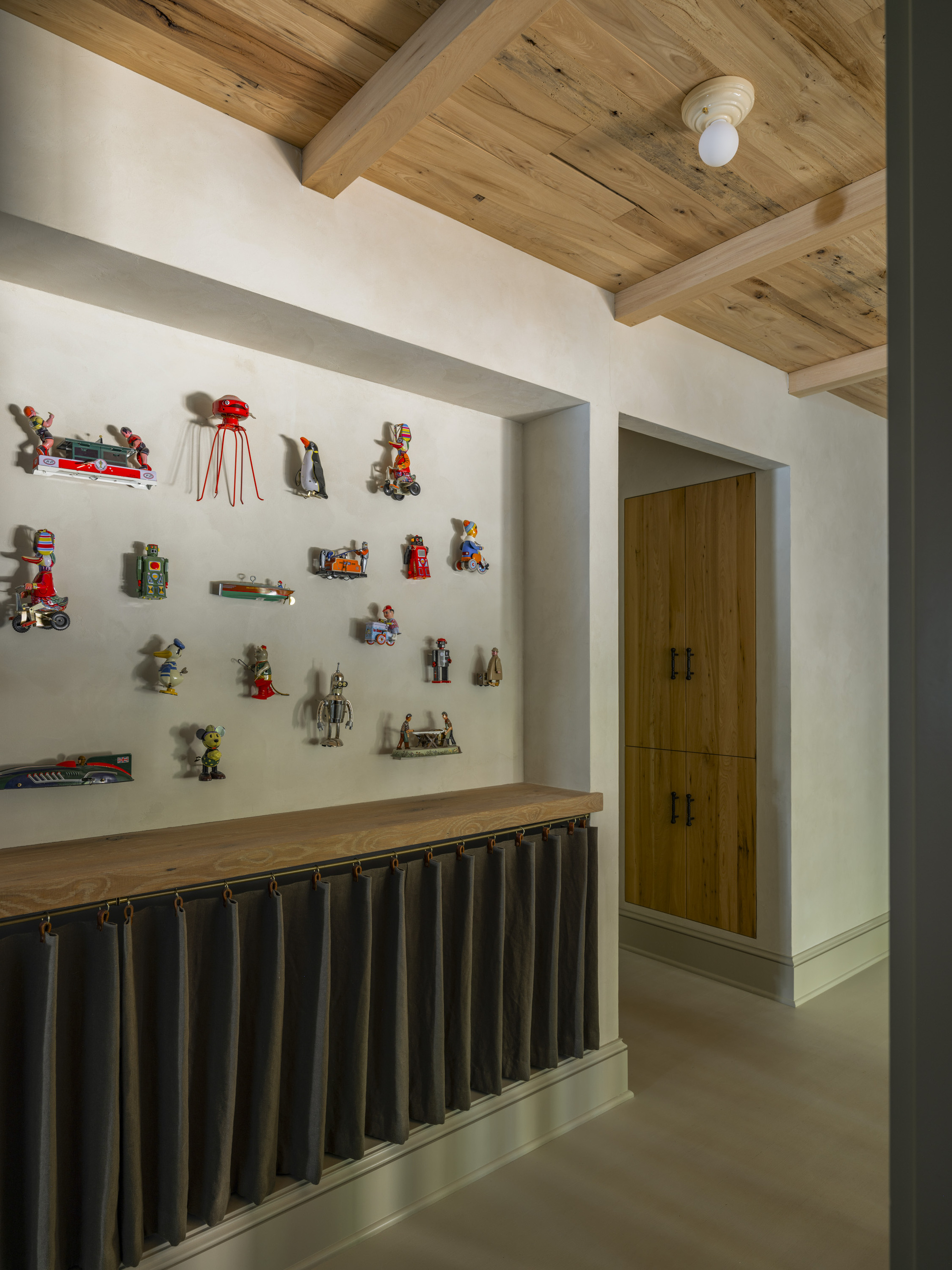 Image of a beige hallway with wooden ceilings. There are vintage toys hung on the wall.