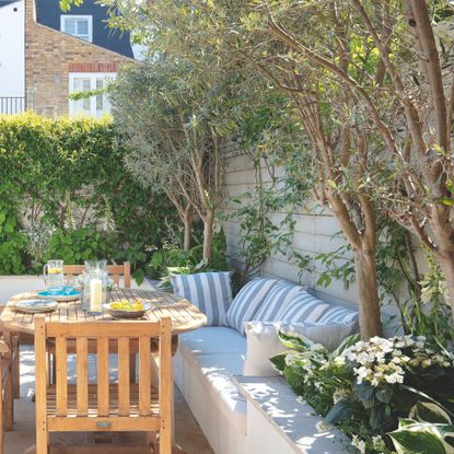 Wooden garden seating area surrounded by garden border with raised planters and trees