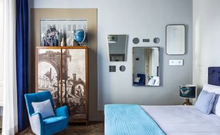 Bedroom featuring decorated wardrobe, blue chair and different shaped mirrors on the wall