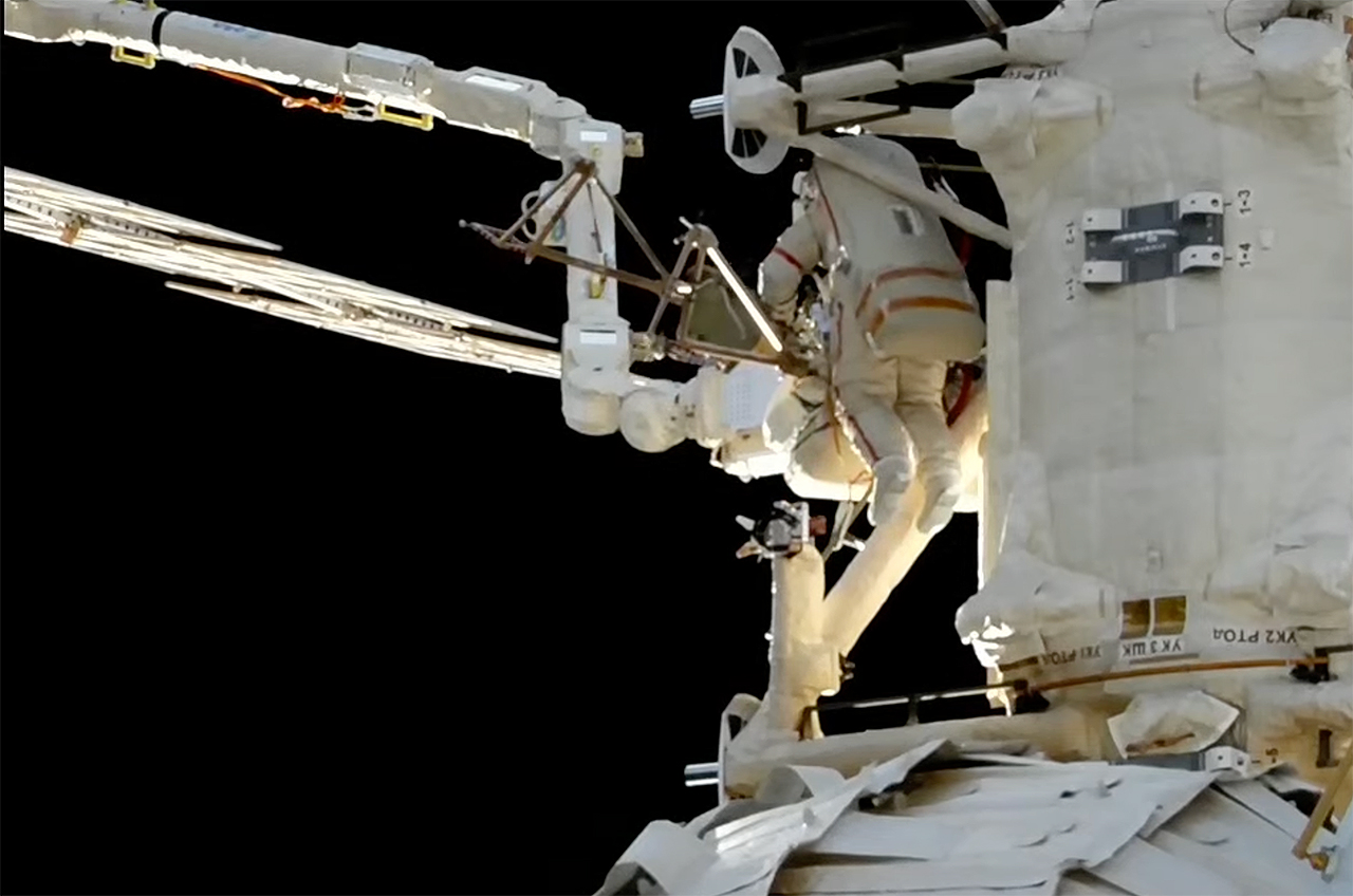 a spacewalking astronauts works outside the international space station with the blackness of space in the background