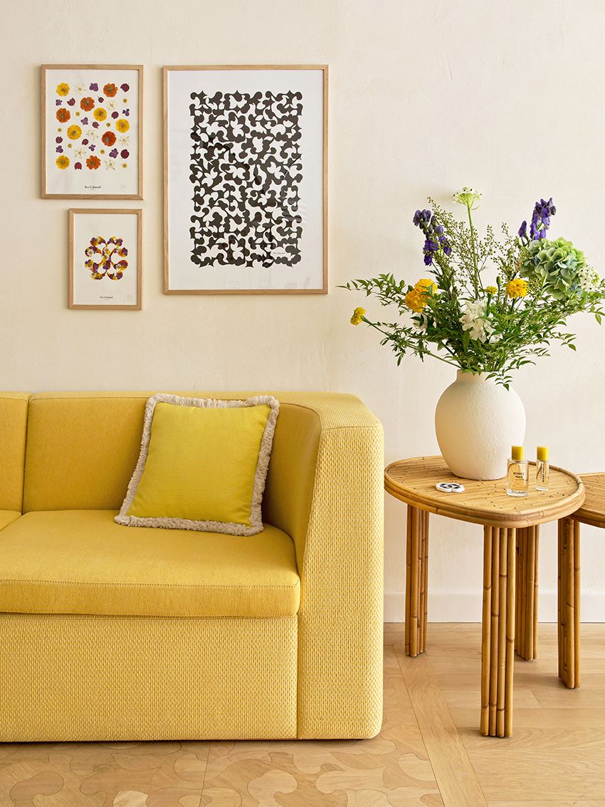 A boutique features an upholstered yellow sofa, wall art, flowers in a vase sitting on a rattan side table, and tiled floors.