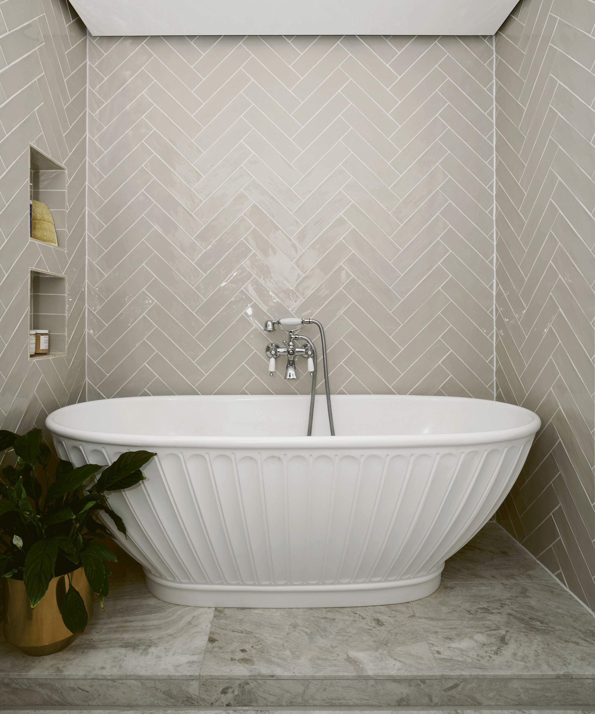 A white freestanding bath with herringbone wall tiles