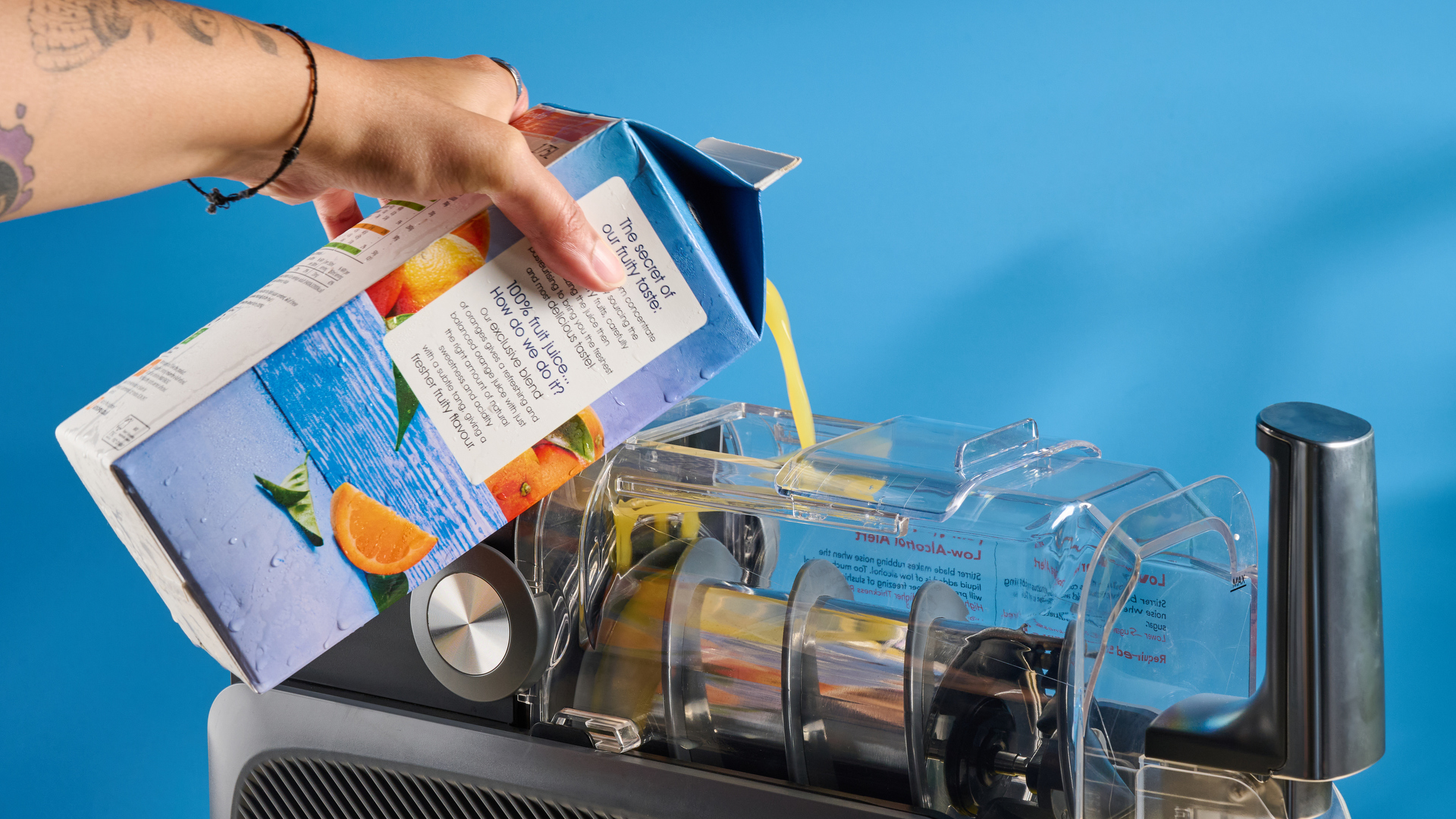 the inoviva slushie machine, a slushie maker with a plastic cylinder body, a dispensing spout, photographed making orange juice slush against a blue tom&#039;s guide background