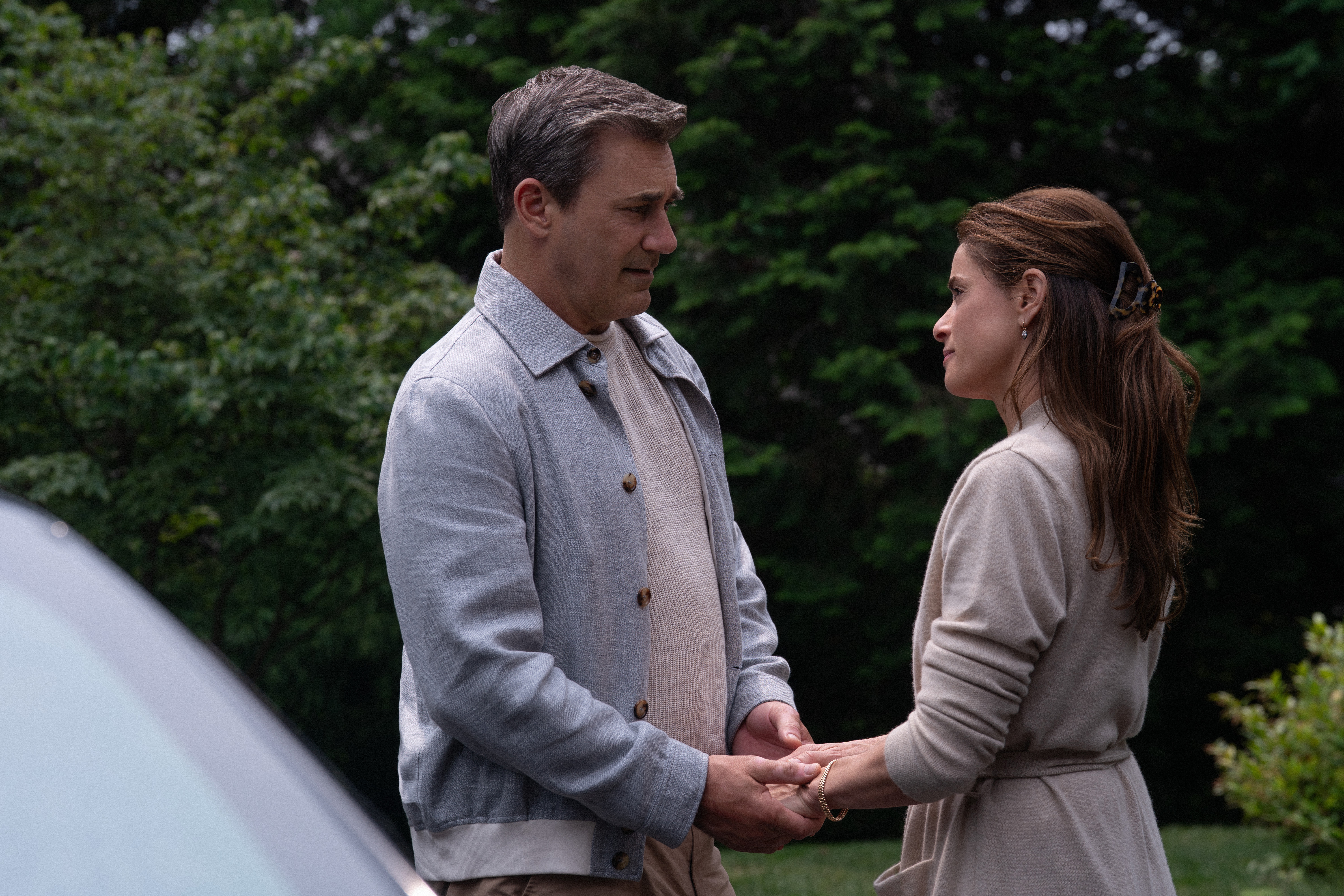 jon hamm as andrew coop cooper and amanda peet as mel cooper holding hands outside on a driveway in your friends and neighbors season 2