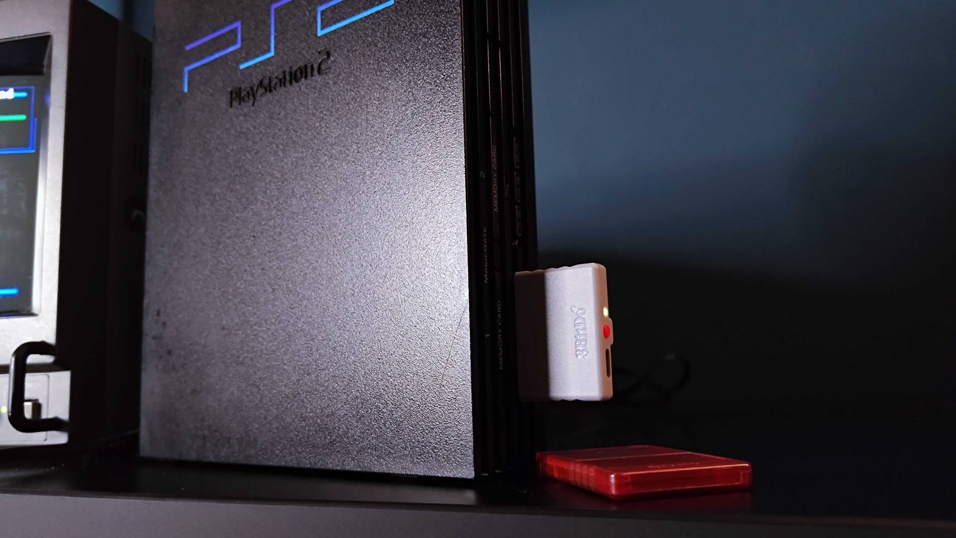 Close up of 8Bitdo Retro Receiver for PS1 and PS2 inserted into controller port with red memory card lying below on black desk.