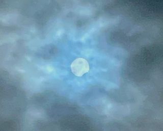 A blue-toned, cloudy sky with a white sun behind the clouds. It looks like a bite was taken out of the bottom right.