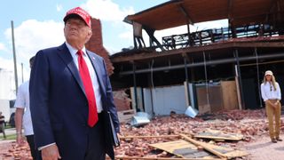 Donald Trump walks through the wreckage from a hurricane wearing a MAGA hat