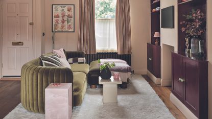 Plaster pink living room with burgundy built-in alcove cupboards and a green velvet corner sofa sitting on a beige rug