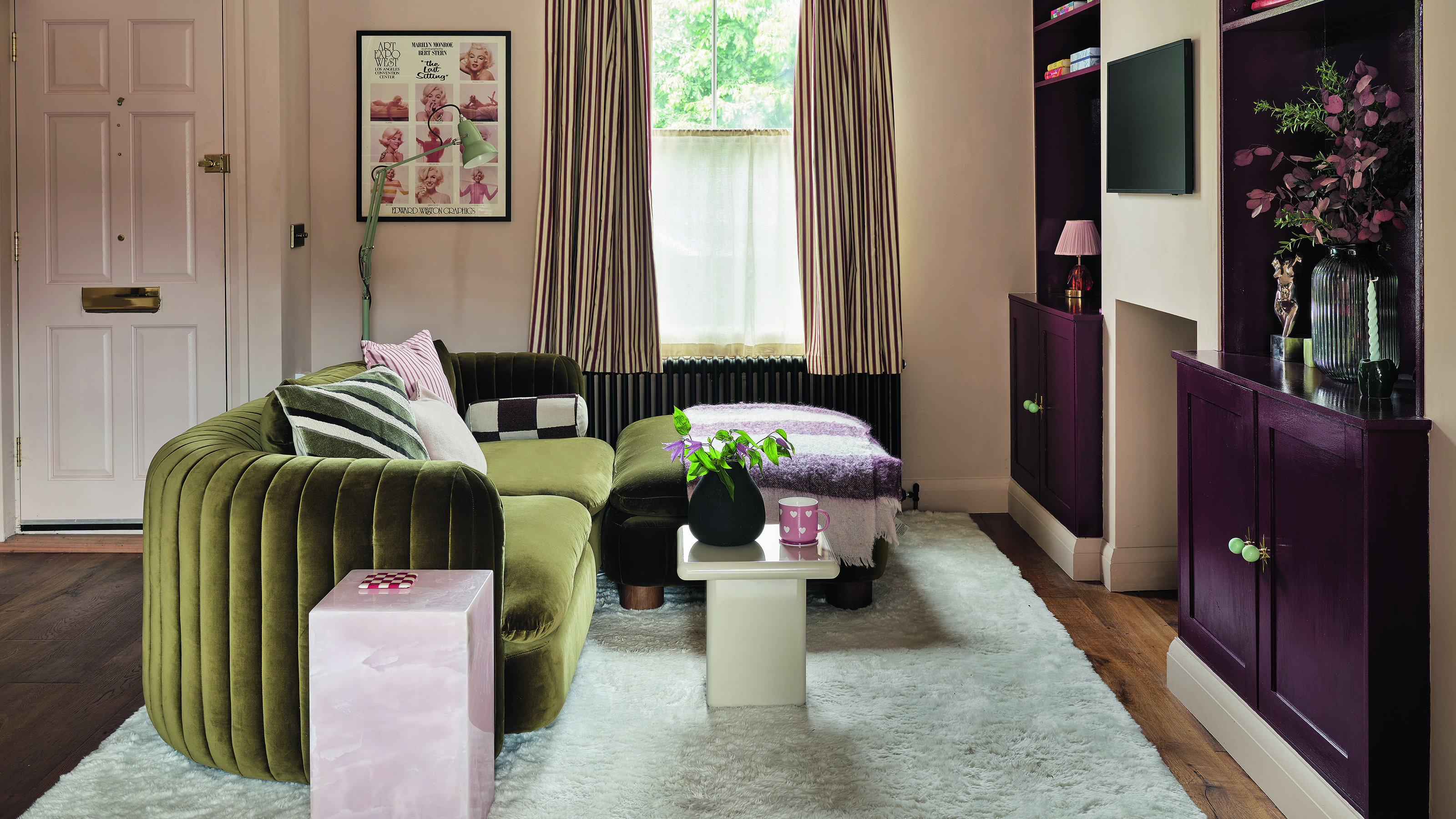 Plaster pink living room with burgundy built-in alcove cupboards and a green velvet corner sofa sitting on a beige rug