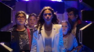 Still from the movie Blue Beetle (2023). Group of 5 main characters walking through doors (daughter, mother, grandmother, and father being lead by an adult woman in a white suit).
