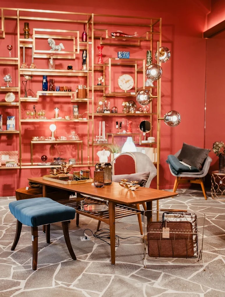 A coral-hued room filled with collectibles placed on a brass shelving unit, mid-century modern furniture, and more.