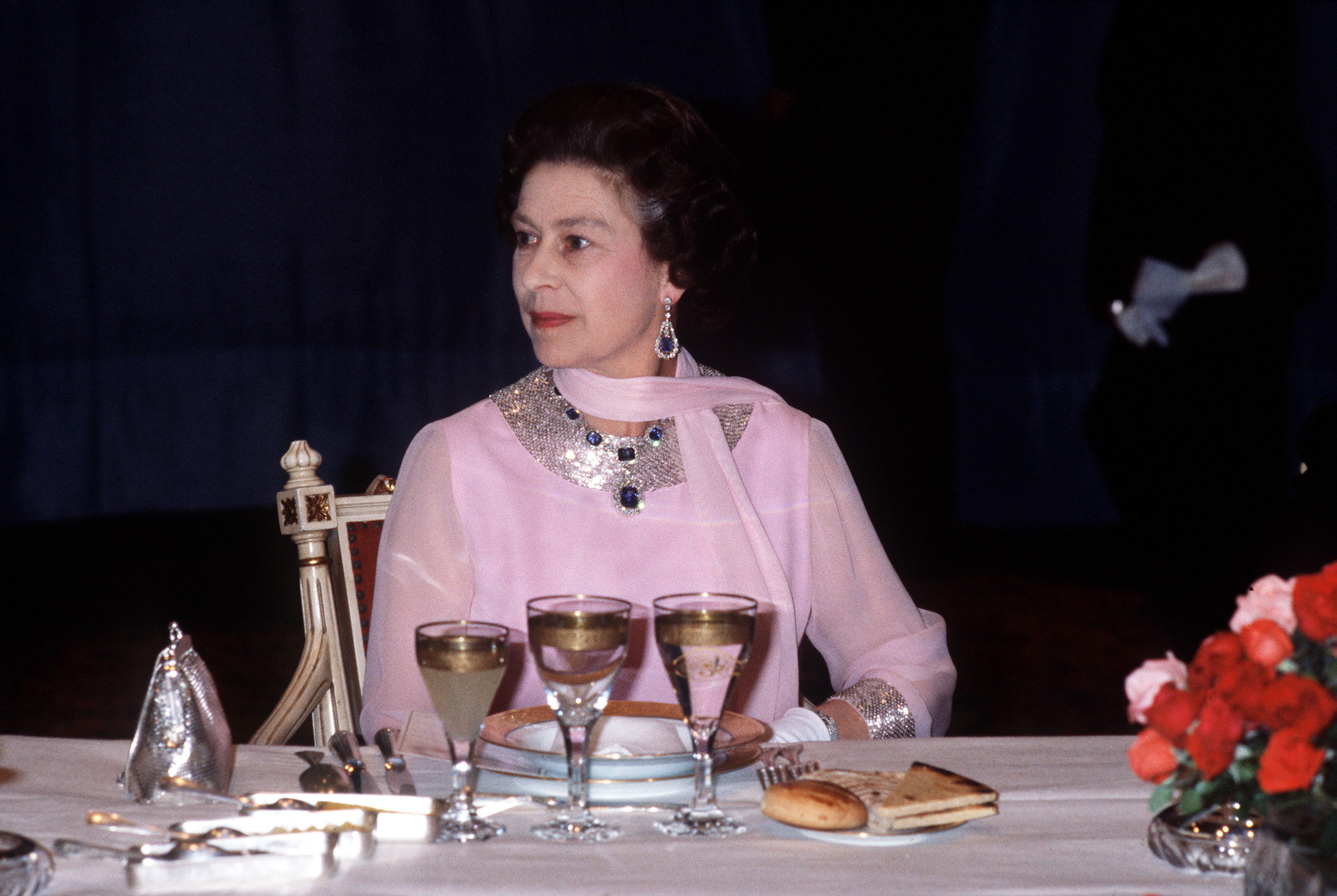 Queen Elizabeth wearing a pink dress sitting at a table