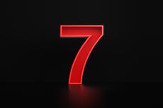 Red number seven sitting on a black background. 