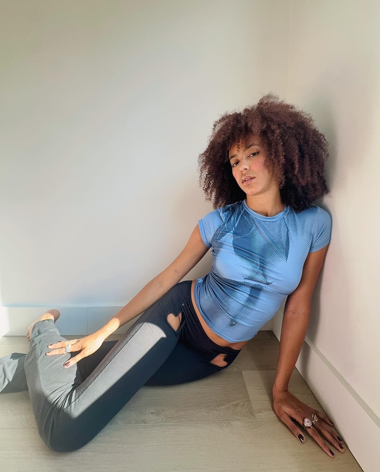 A woman sitting on the floor in loungewear with a curly, shaggy lob hairstyle
