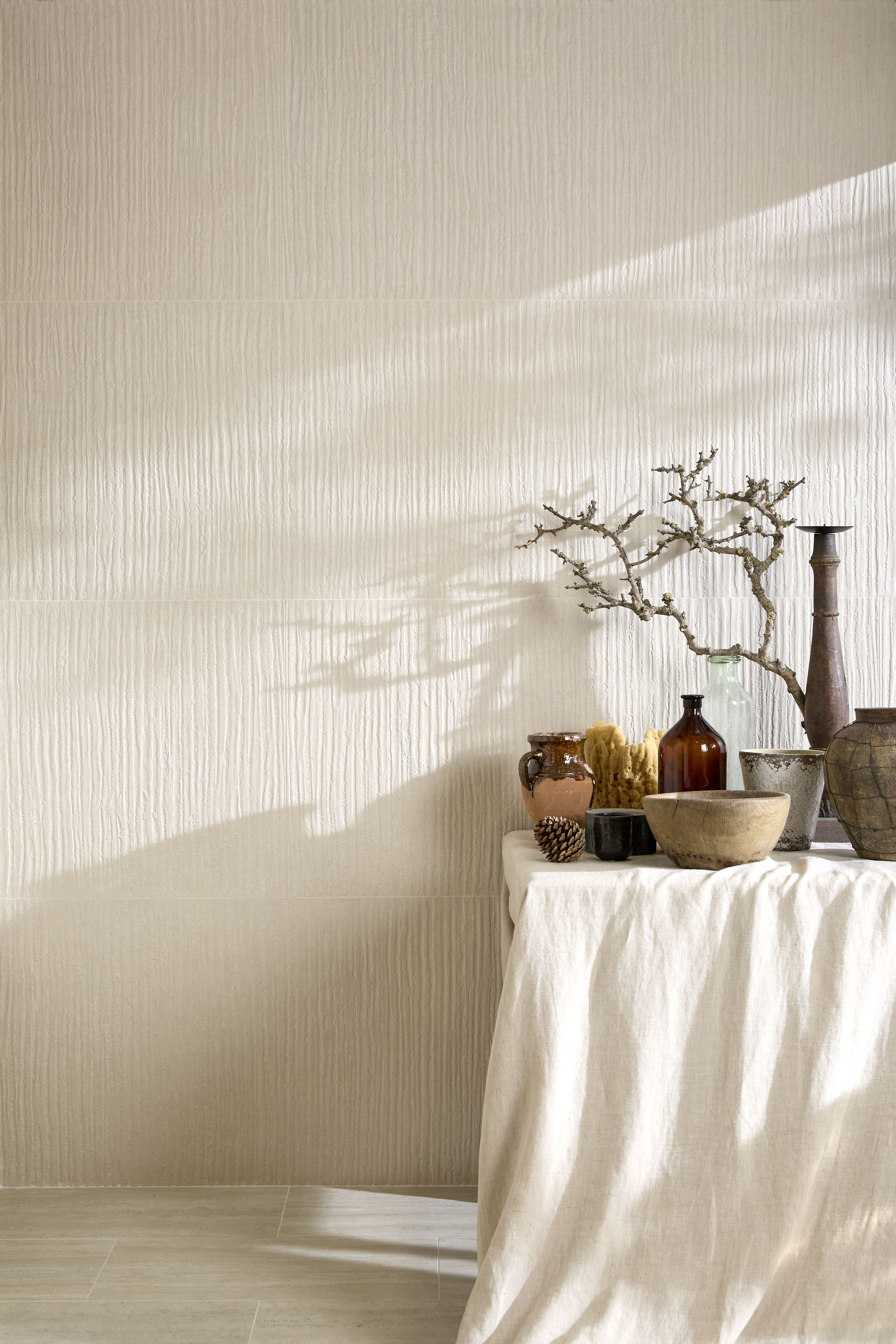Image of a white wall that is made of plaster tile with a white table in front of it with lots of ceramic vases on it.