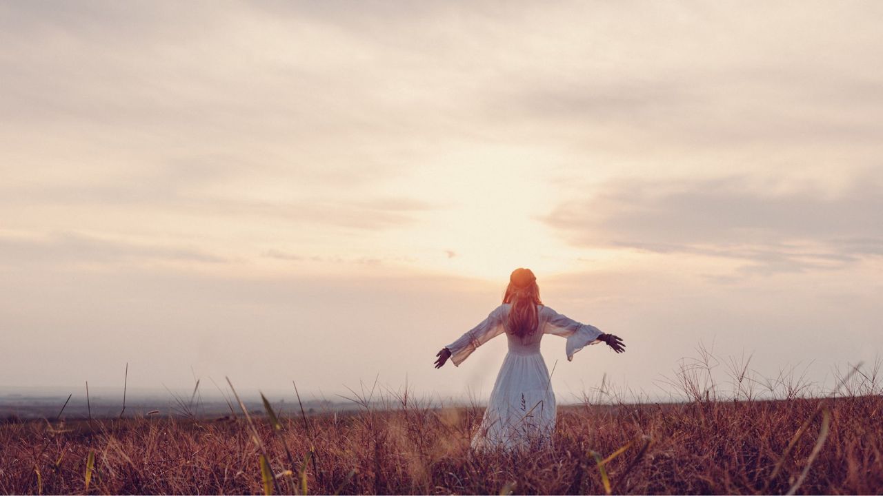 A woman, standing in a meadow at sunset