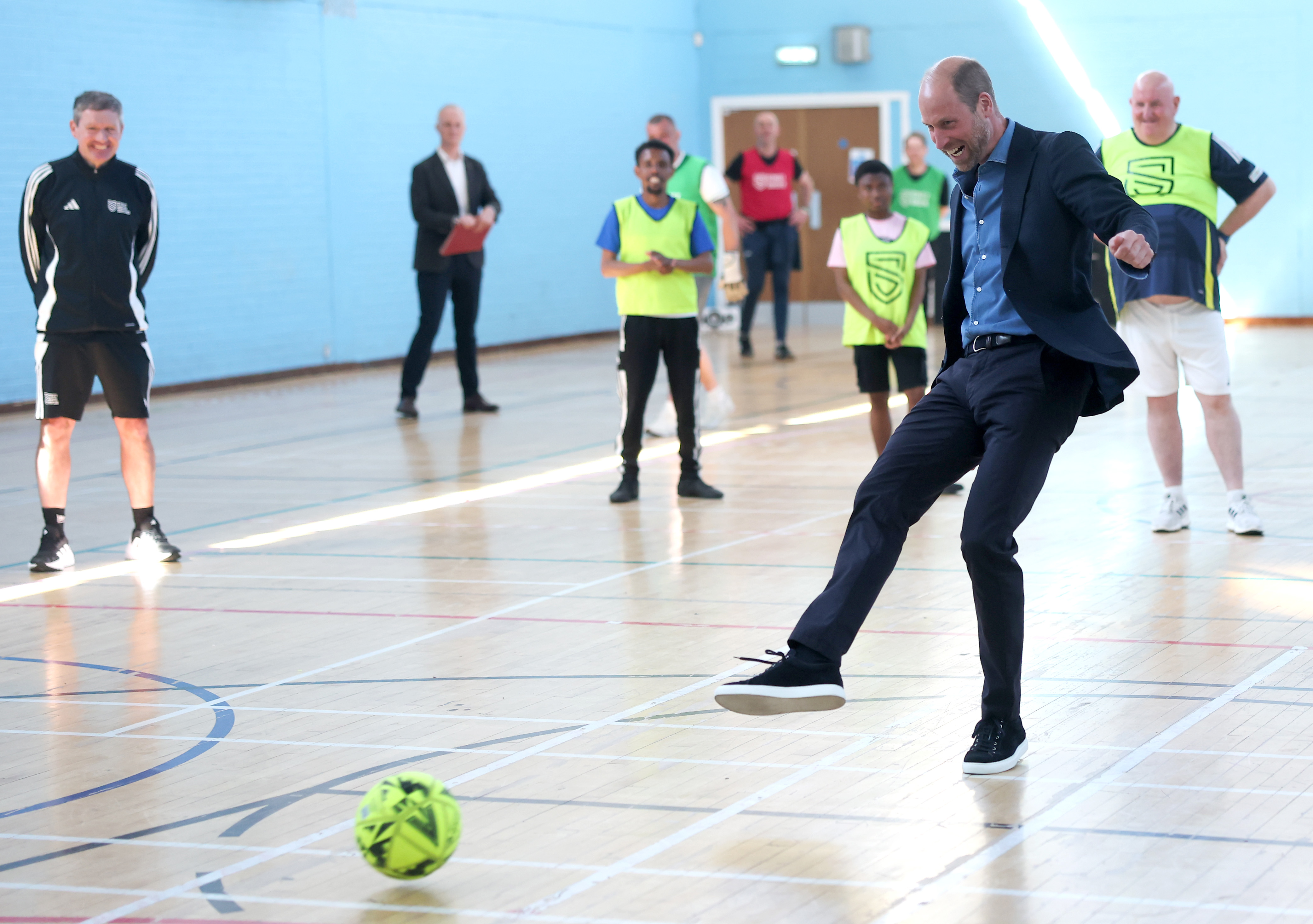 Prince William kicking a soccer ball in a suit