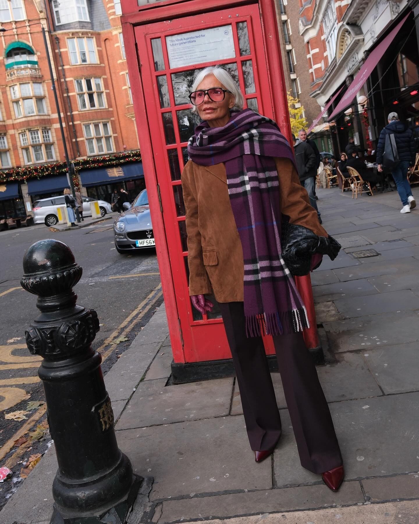 Grece wears a purple check scarf, suede jacket, brown pants, and burgundy shoes.