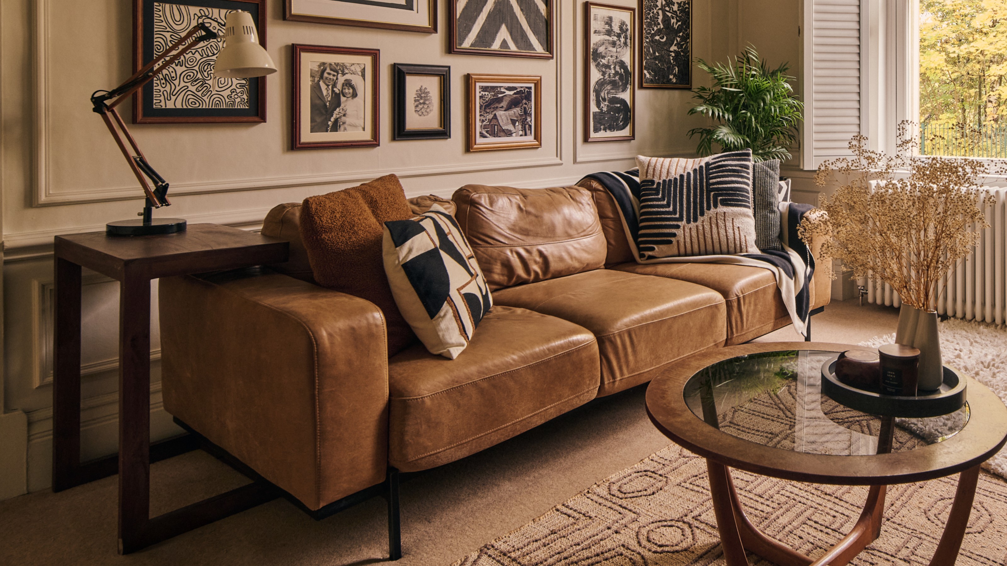 A living room with a three-seater brown leather sofa on narrow black metal legs and a gallery wall above it